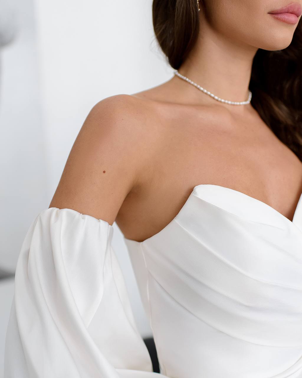 Close-up of a person wearing a white off-shoulder dress with a plain background