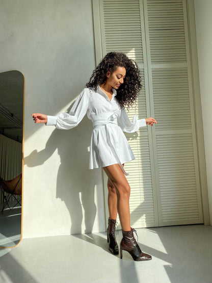 Woman in a white dress standing against a light-colored wall.