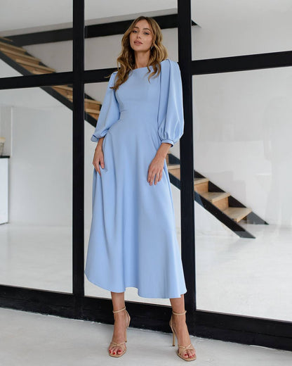 Woman wearing a light blue dress standing in a modern interior setting with stairs.
