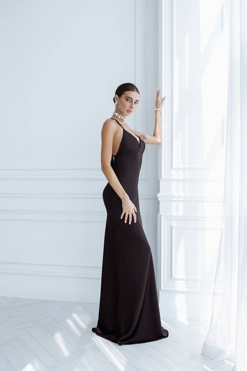 Woman in a black evening gown standing against a white wall.