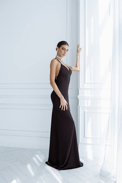 Woman in a black evening gown standing against a white wall.