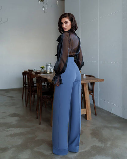 Woman in a black sheer top and blue pants standing in a dining room.