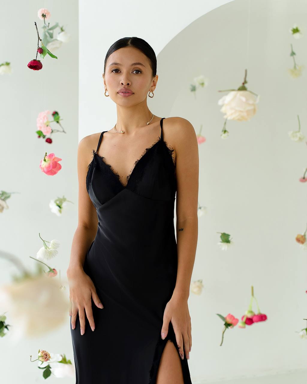Woman wearing a black slip dress with floral decorations in the background