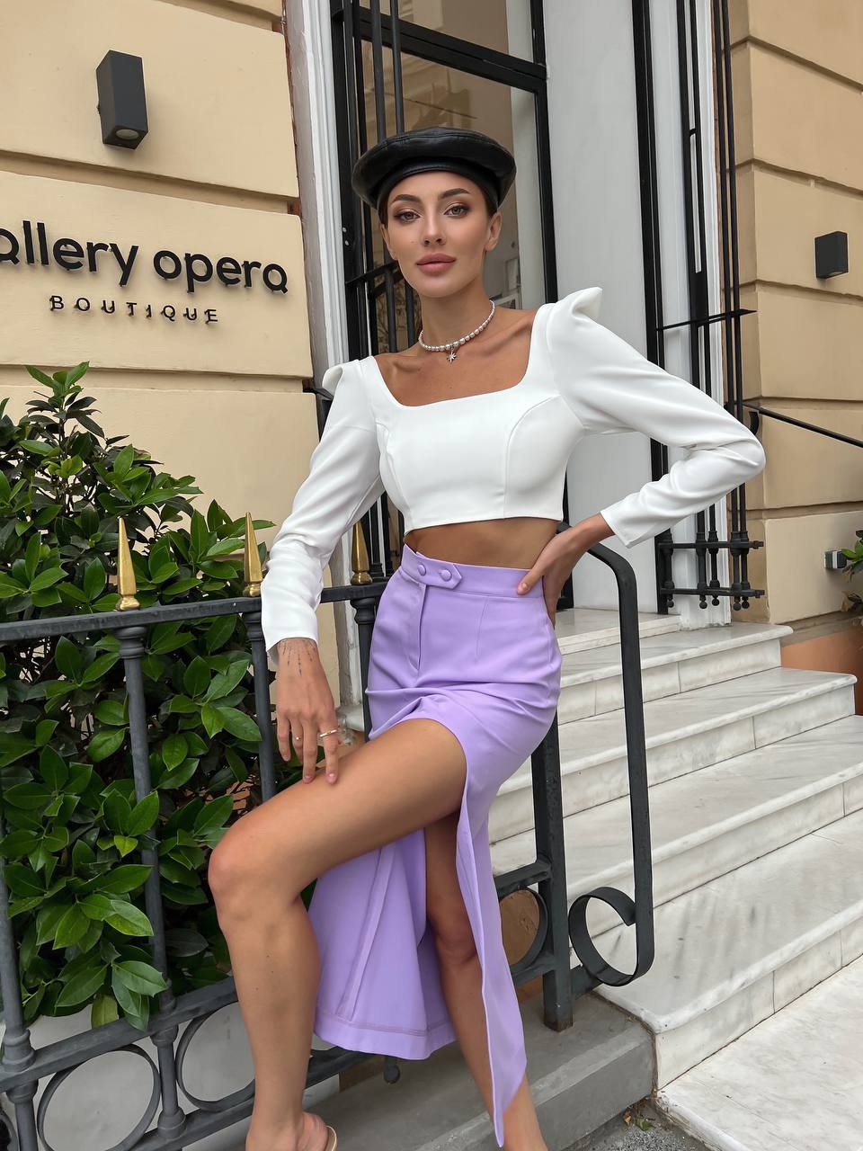 Woman in white top and purple skirt posing in front of Gallery Opera Boutique.