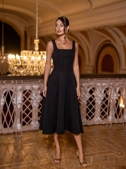 Woman in a black dress standing in an elegant indoor setting with chandeliers.