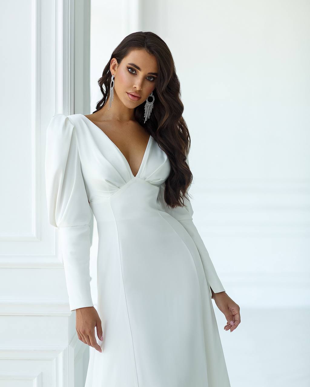 Woman wearing a white wedding dress with long sleeves in a bright room.