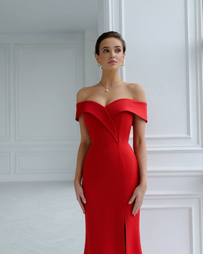 Woman wearing a red off-shoulder dress against a white paneled wall.