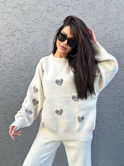 Woman wearing a cream sweater with heart patterns against a gray wall