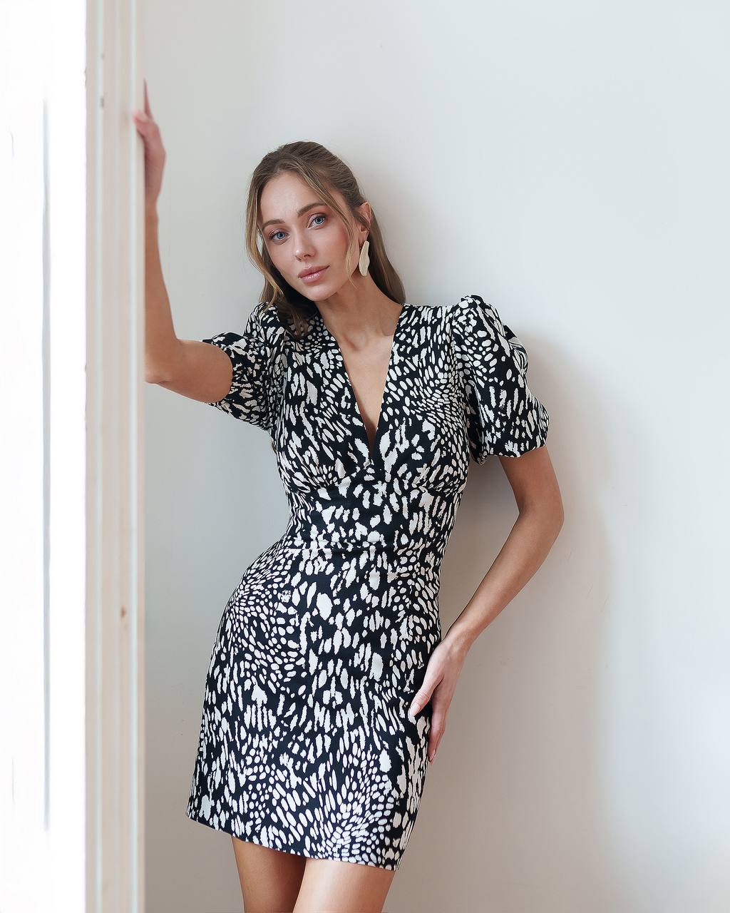 Woman wearing a black and white patterned dress against a plain wall.