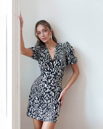 Woman wearing a black and white patterned dress against a plain wall.