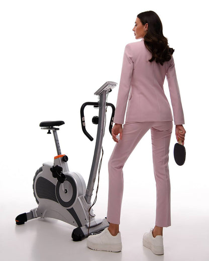 Woman in a pink suit standing next to an exercise bike on a white background