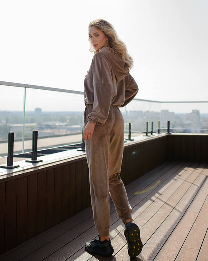 Woman in a beige tracksuit standing on a rooftop with a cityscape view.
