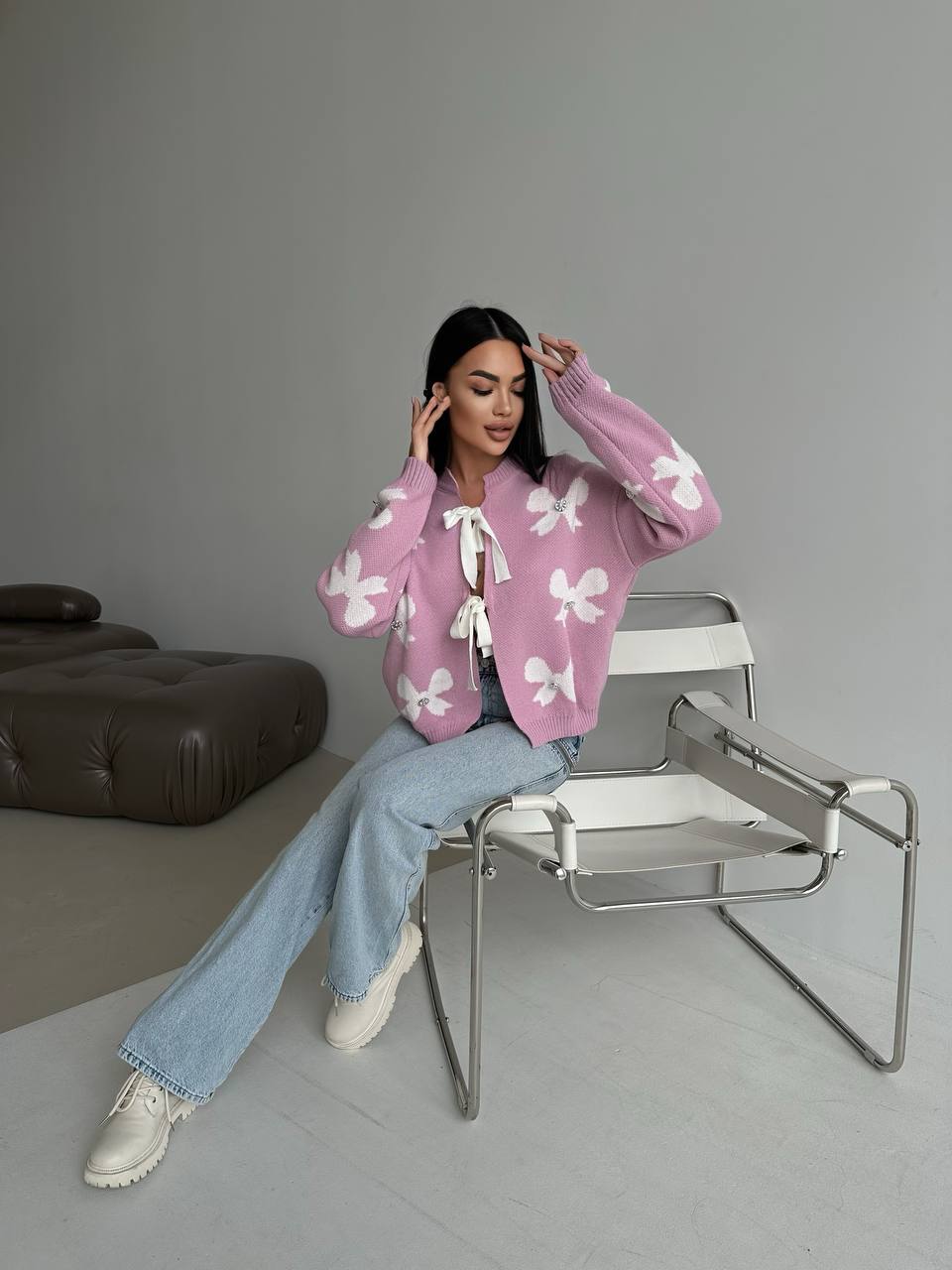 Woman wearing a pink cardigan with white butterfly patterns, sitting on a modern chair in a minimalistic room.