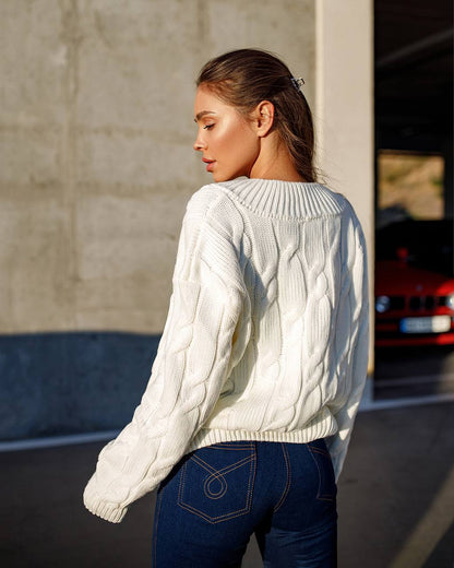 Person wearing a white cable knit sweater and blue jeans standing outdoors.