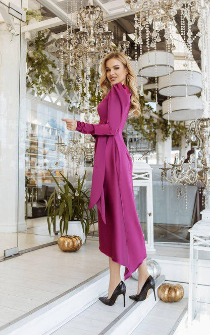 Woman in a pink dress standing in an elegant interior setting with chandeliers and plants.