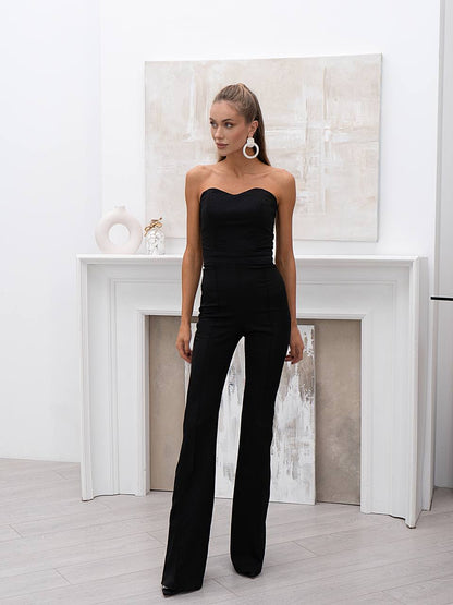 Woman wearing a black strapless jumpsuit in a minimalistic room with a fireplace.