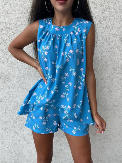 Woman wearing a blue floral top and shorts set against a gray background
