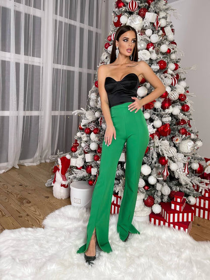 Woman in a black top and green pants standing in front of a decorated Christmas tree with presents.