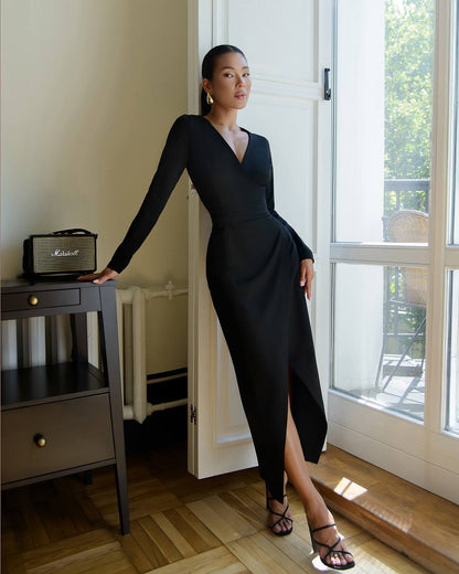 Woman in a black dress standing in a room with a window and furniture.