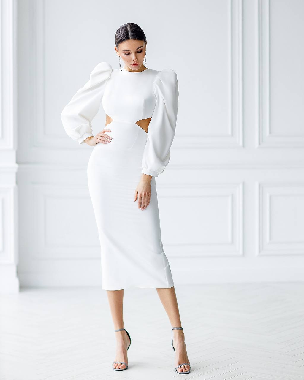 Woman wearing a white dress with cut-out design against a white wall