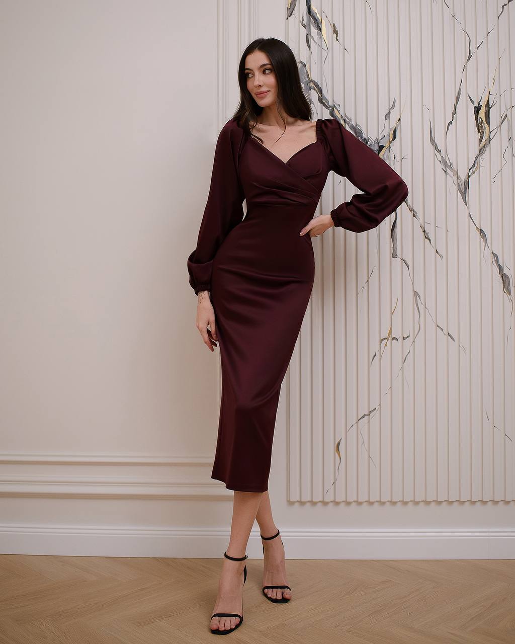 Woman wearing a burgundy dress standing against a marble wall.