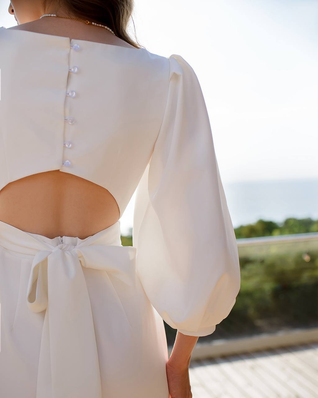 White dress with open back and long sleeves, blurred outdoor background