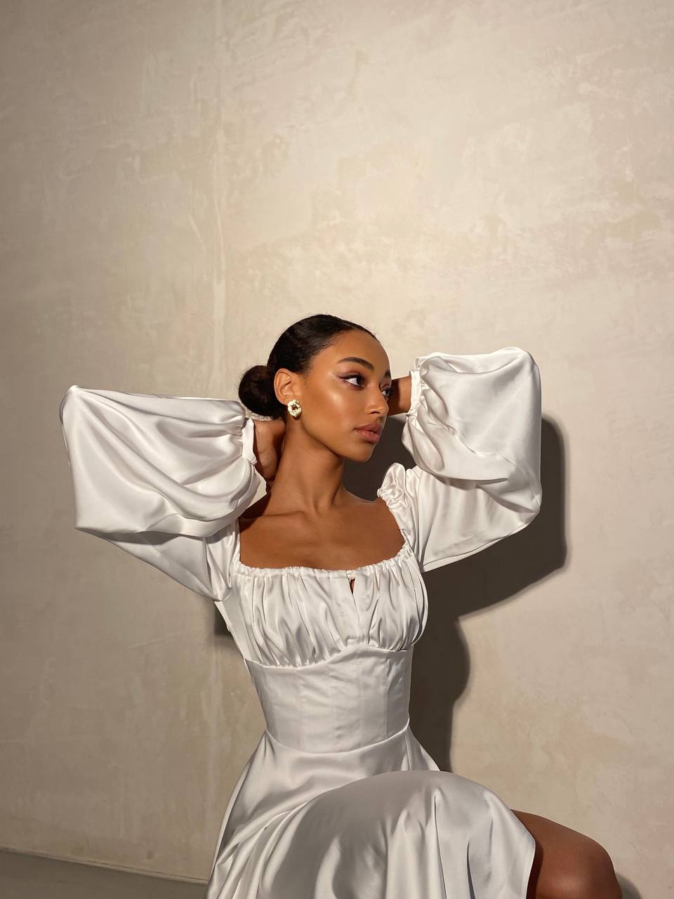 Woman in a white dress with puffed sleeves against a plain background