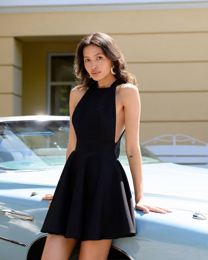Woman in a black dress leaning on a classic car with a yellow building in the background