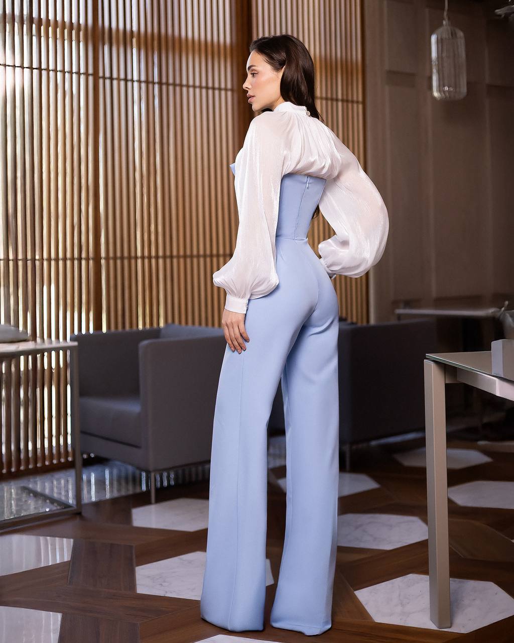 Woman in a white blouse and light blue pants standing in a modern interior setting.