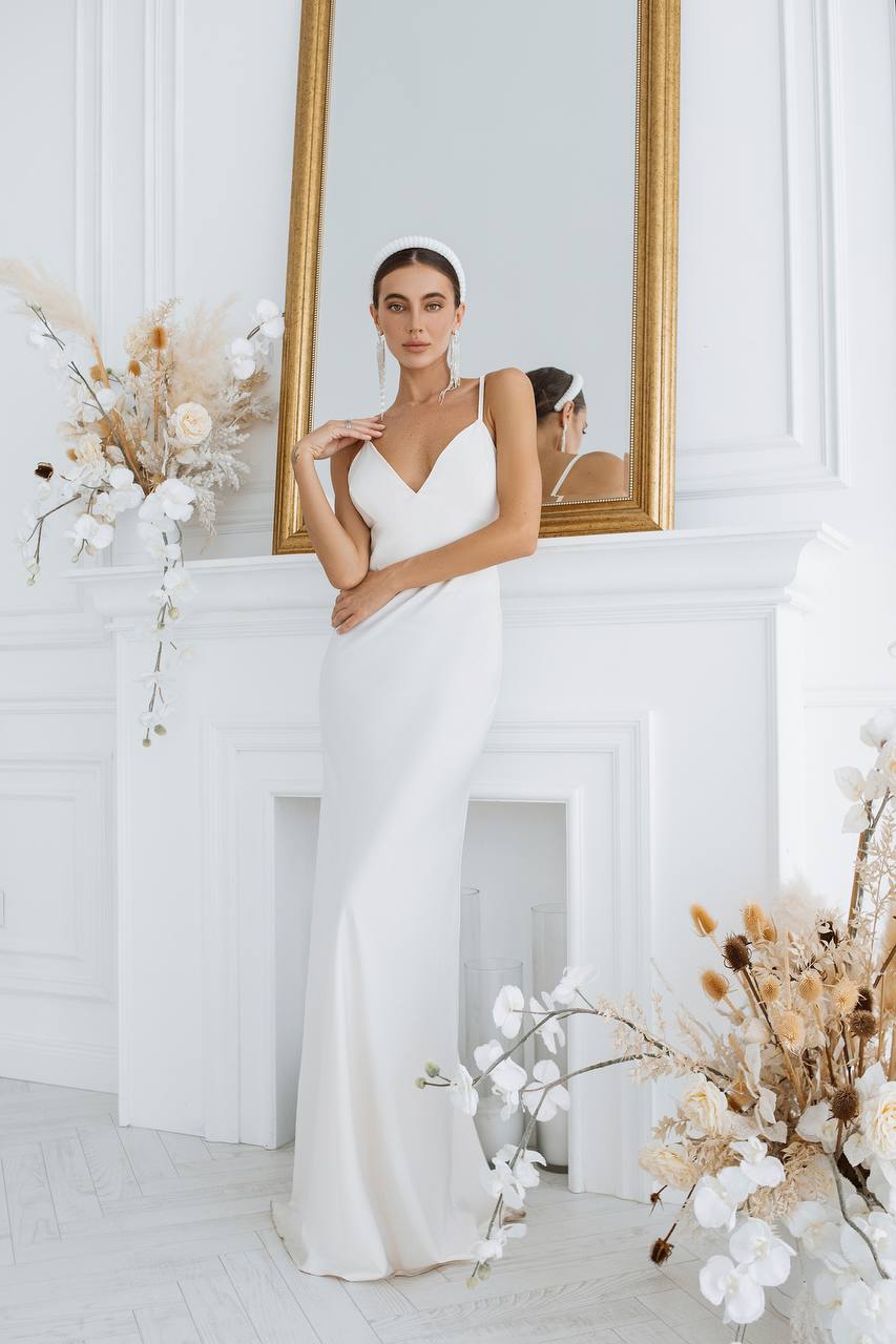 Woman in a white wedding dress standing in front of a mirror with floral decorations.