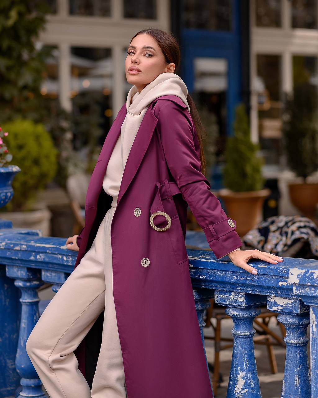 Woman in a long purple coat standing outdoors near a blue railing.