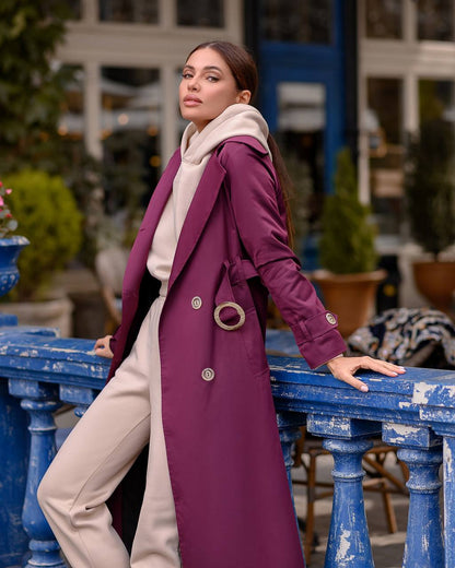Woman in a long purple coat standing outdoors near a blue railing.