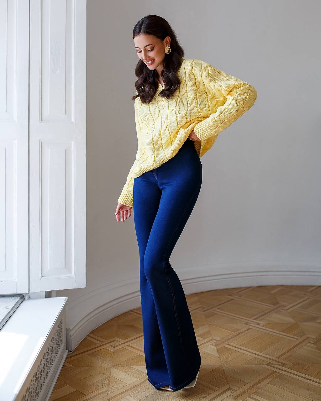 Woman wearing a yellow sweater and blue pants in an indoor setting.