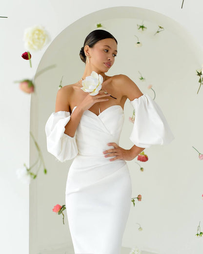 Woman wearing a white off-shoulder dress with floral decorations in the background