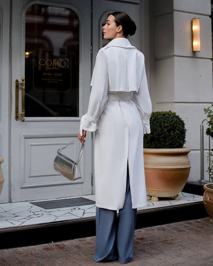 Woman in a white coat standing in front of a building entrance.