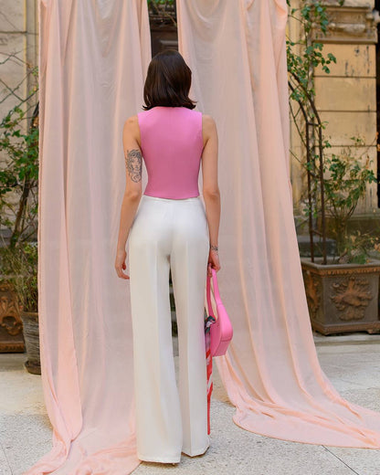 Person wearing a pink top and white pants standing in front of sheer curtains.