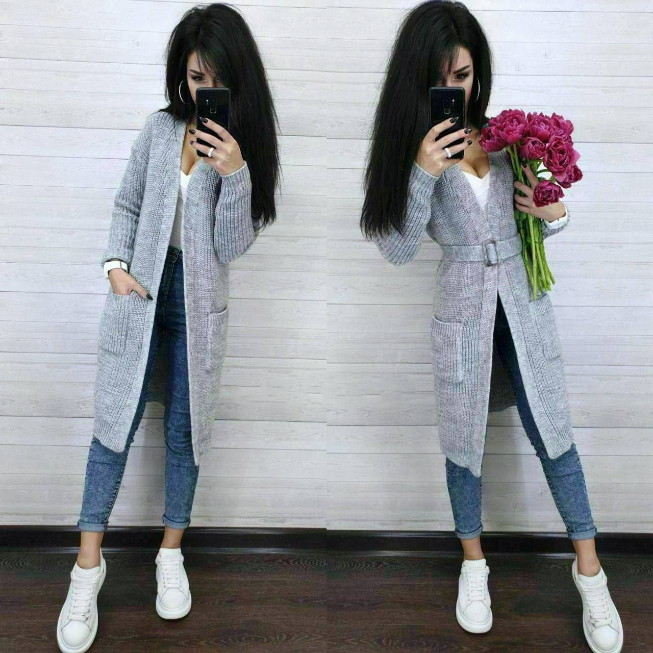 Woman taking a mirror selfie wearing a long gray coat, white shirt, blue jeans, and white sneakers.