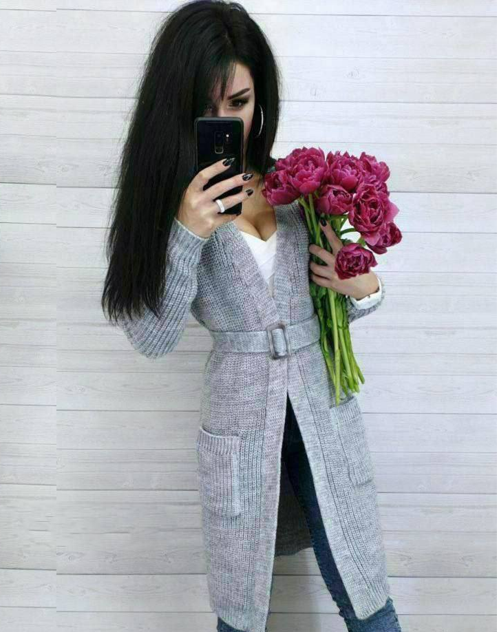 Woman in a long gray coat holding pink flowers against a light wooden panel background