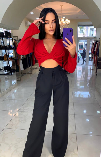 Woman taking a mirror selfie wearing a red top and black pants in a store.