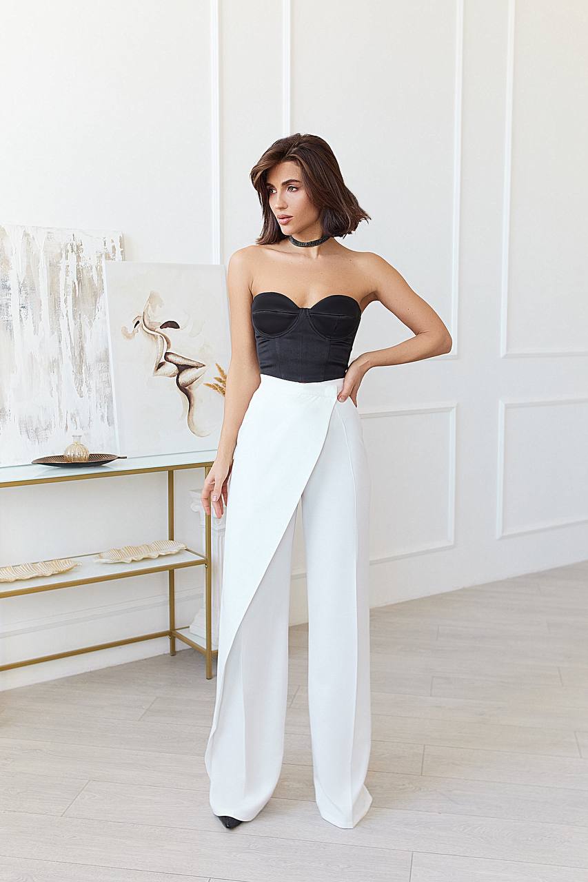 Woman wearing a black strapless top and white pants in a minimalistic room.