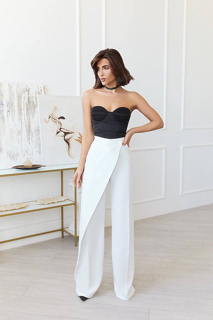 Woman wearing a black strapless top and white pants in a minimalistic room.