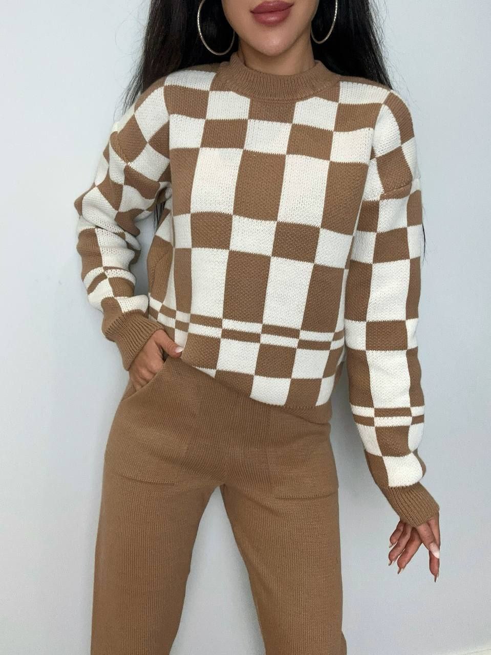 Person wearing a brown and white checkered sweater with matching pants against a plain background
