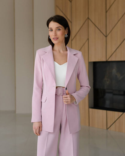 Woman wearing a light pink suit standing in a modern interior setting.