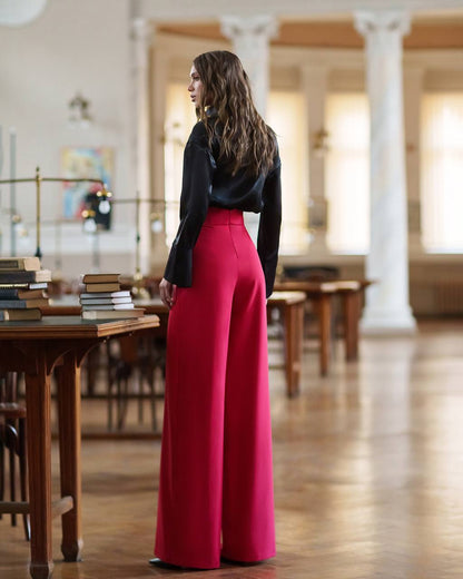 Woman wearing a black top and red pants standing in a library.