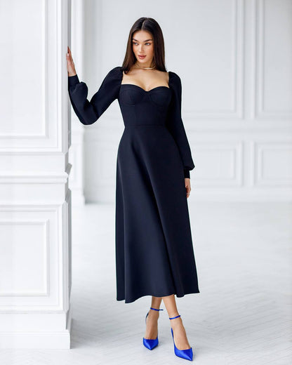 Woman wearing a black dress with long sleeves in a white room.