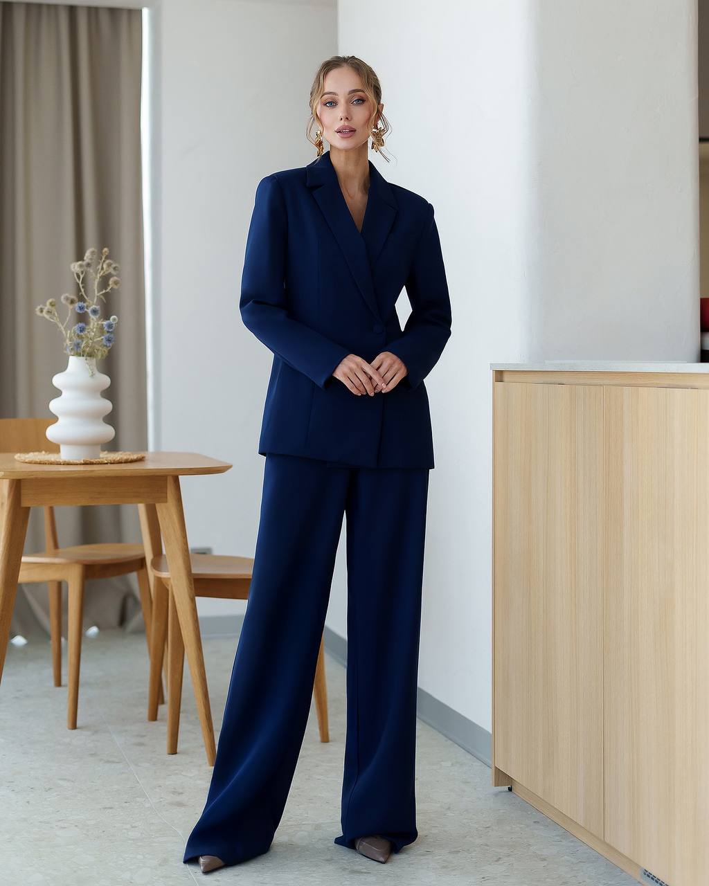 Woman in a navy blue suit standing in a modern interior setting.