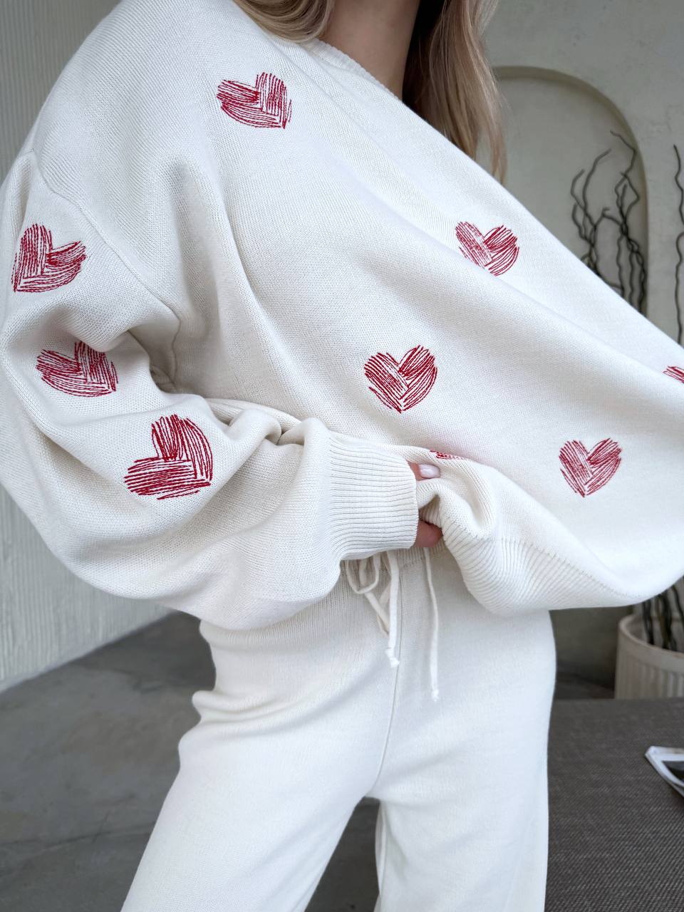 White sweatshirt with red heart patterns worn by a person indoors.