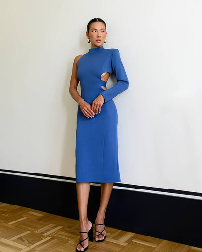 Woman wearing a blue dress with cut-out design against a white wall.