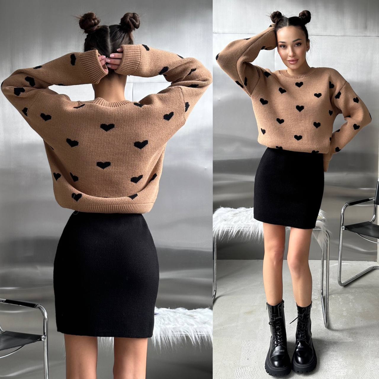 Woman wearing a beige sweater with black heart patterns and a black skirt indoors.