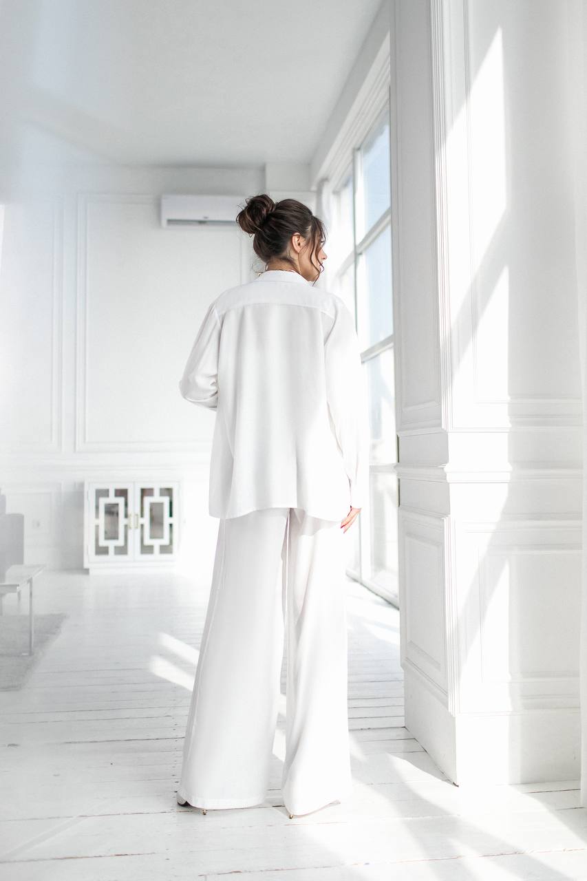 Person wearing a white outfit standing in a bright, minimalistic room.